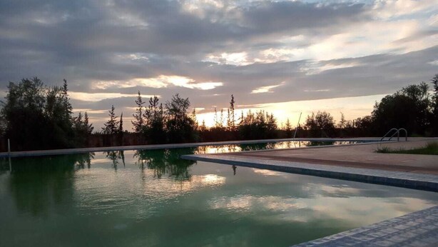 Ein Schwimmbecken mit einer gefliesten Kante, umgeben von Bäumen und einem bewölkten Himmel.