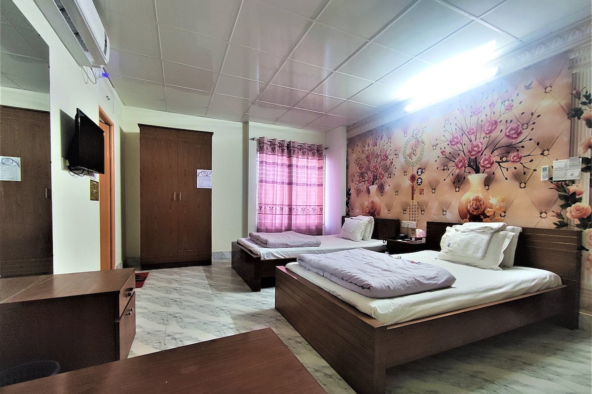 A hotel room with two single beds, a wooden wardrobe, a desk, and a television.