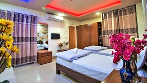 A hotel room with two beds, a ceiling light, a TV, and a vase with flowers. - HOTEL PUSHPO BILASH (Khulna)