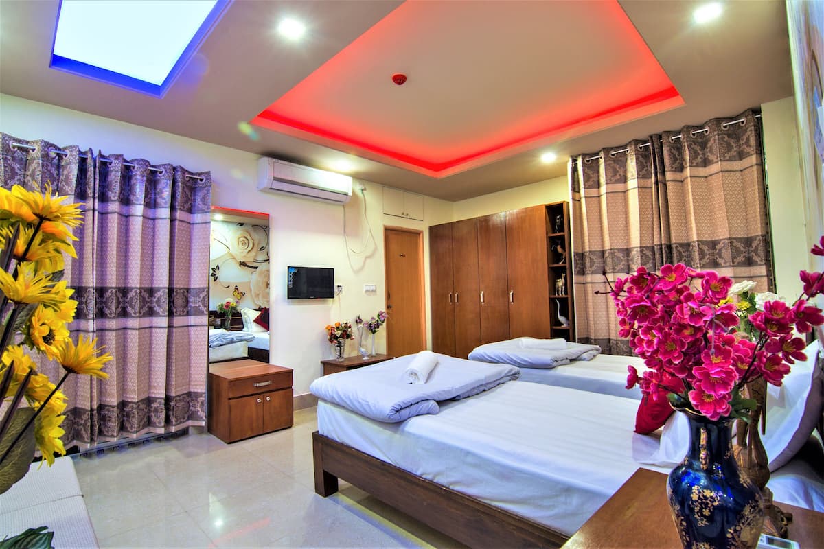 A hotel room with two beds, a ceiling light, a TV, and a vase with flowers.