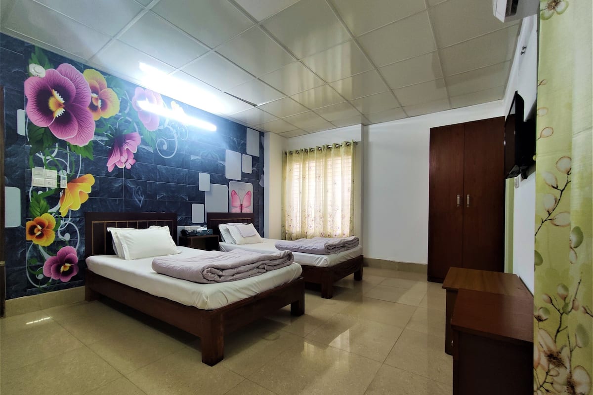 A hotel room with two beds, a flat-screen TV mounted on the wall, and a floral-patterned curtain.