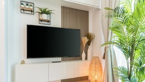 A modern living room with a flat-screen TV mounted on a white cabinet, a large potted plant, and a decorative vase with pampas grass. - Stunning Apt Marina view with Balcony (Dubai)