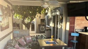 An outdoor patio area with a sofa, chairs, a table with a fire feature, a ceiling fan, and a kitchen area with a bar. - Staycation Home minutes to all Pheonix has to offer (Glendale)