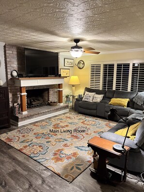 A main living room with a fireplace, a sofa, a TV, and a patterned rug.