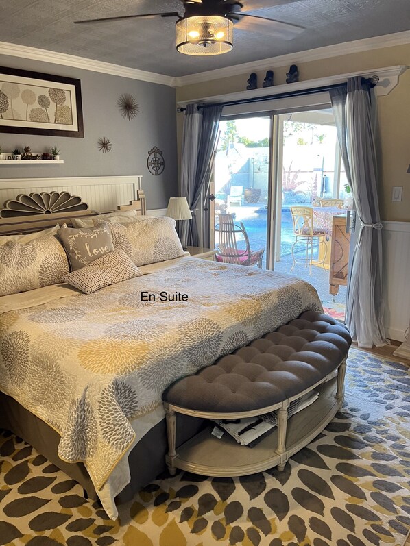 A bedroom with a large bed, a bench, a ceiling fan, and a view of an outdoor patio.