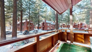 Una terraza de madera con vista a una zona residencial, que incluye casas y coches aparcados.