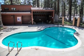 Una piscina con plataforma de madera y zona cubierta con sillas.