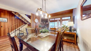 A dining area with a wooden table, chairs, and a potted plant. There is a staircase with wooden railings and a clock on the wall. - Woodlands #11 3 Bedroom Condo by RedAwning (Mammoth Lakes)