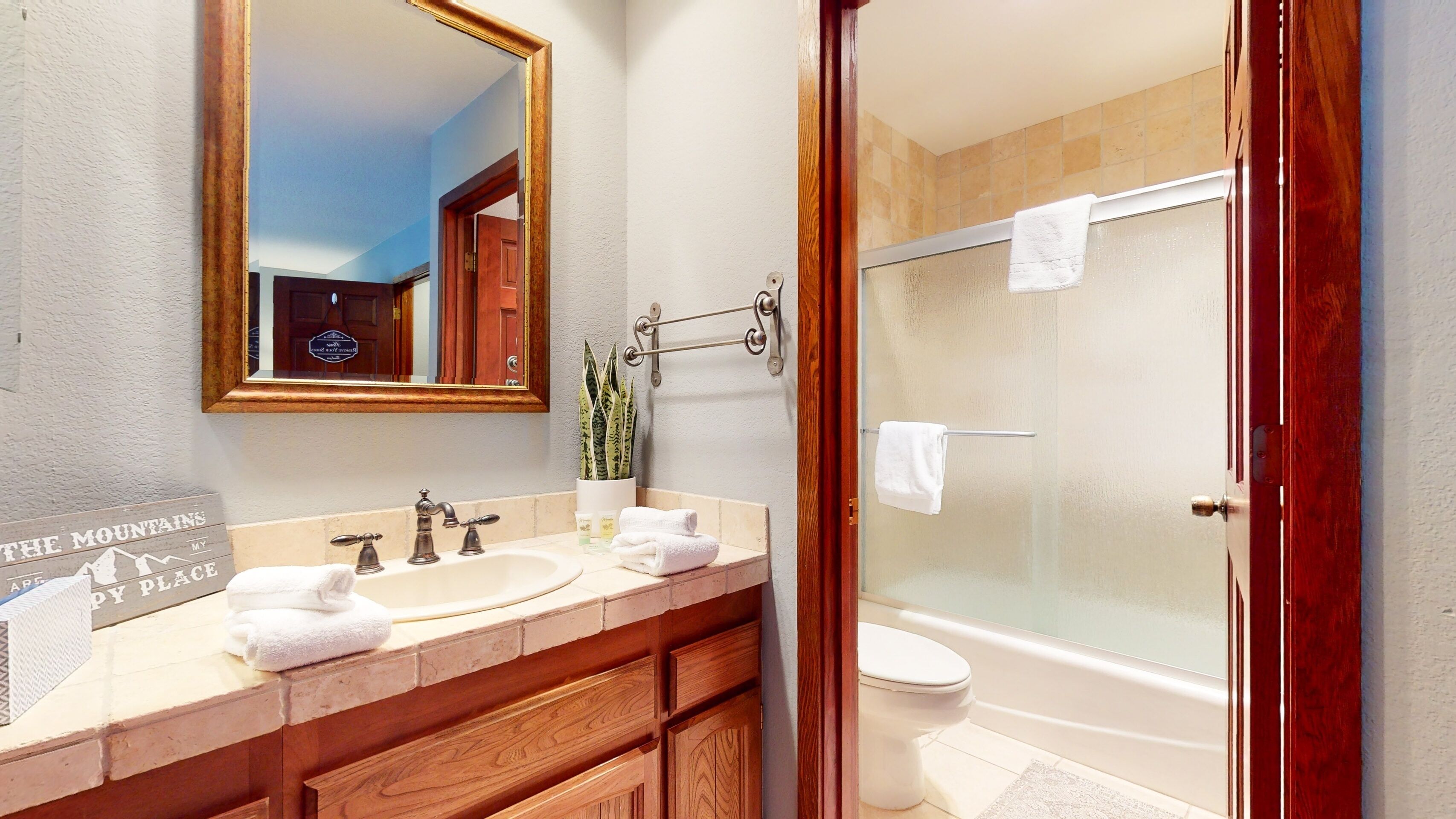 A bathroom with a double sink, a mirror, a towel rack, a potted plant, and a glass-enclosed shower.