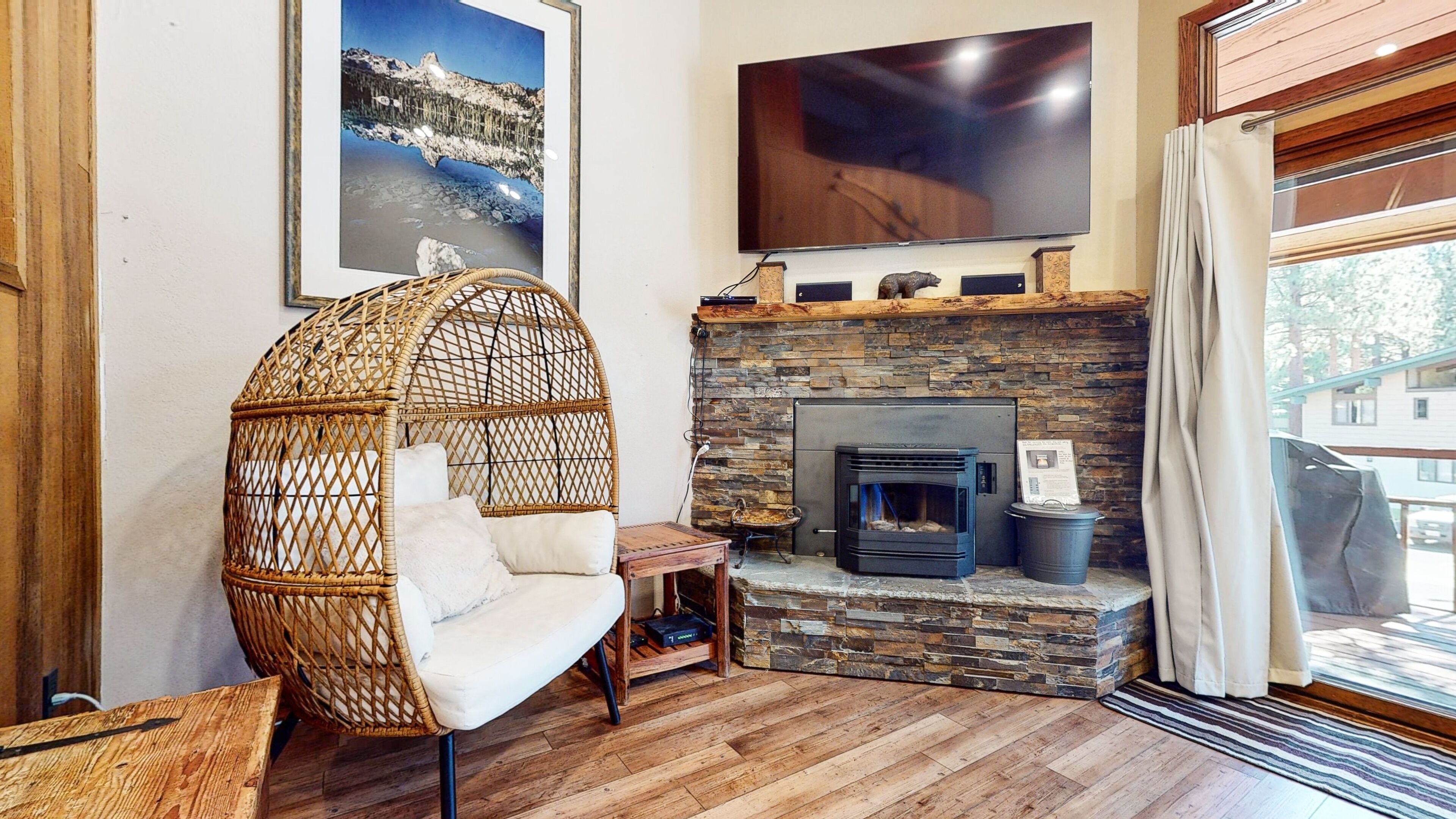 A cozy living room with a stone fireplace, a large flat-screen TV, and a wicker chair.