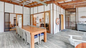 Um quarto espaçoso com uma mesa de jantar de madeira e cadeiras, um ventilador de teto e vista para uma cozinha.