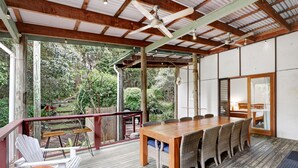 Uma área de refeições coberta ao ar livre, com mesa de madeira e cadeiras de vime, com vista para um jardim.