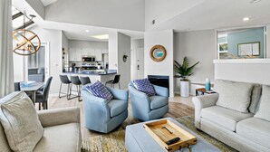 A spacious living room with a sofa, two armchairs, and a coffee table. A kitchen is visible in the background with modern appliances. - Updated 3 bedroom Villa in Shelter Cove with Community Pool (Hilton Head Island)