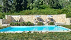 Une piscine aux murs en pierre, dotée d’un espace extérieur aménagé et offrant une vue sur les arbres et les collines.