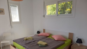 Une chambre à coucher comprenant un lit, des tables de chevet, une chaise, une fenêtre et une étagère fixée au mur.