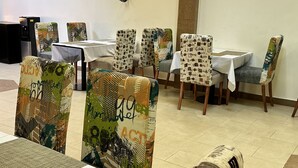 Et spiseområde med mønstrede stole og borde, en central søjle og en loftlampe.