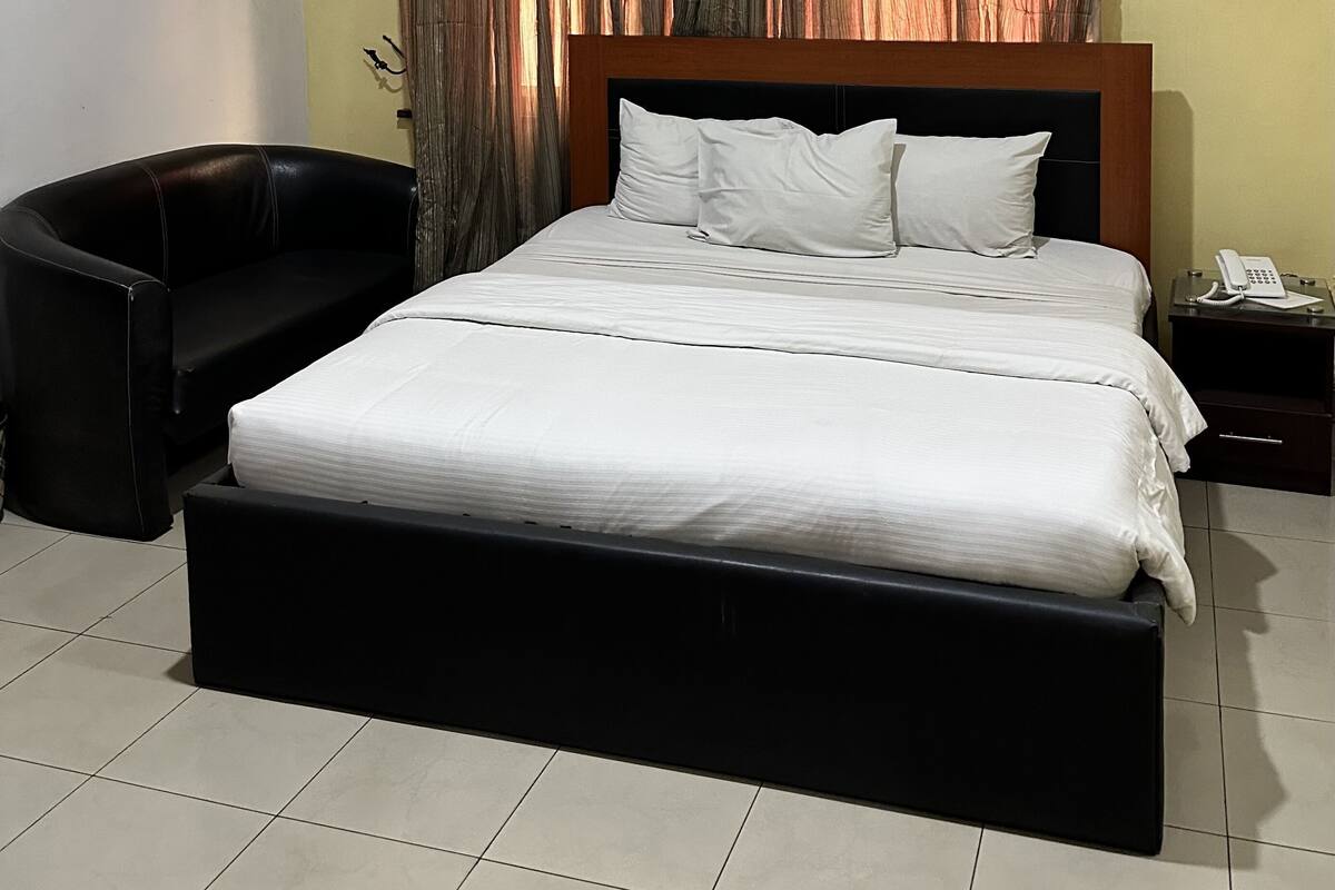 A neatly made bed with white bedding, a black headboard, and a bedside table with a telephone.