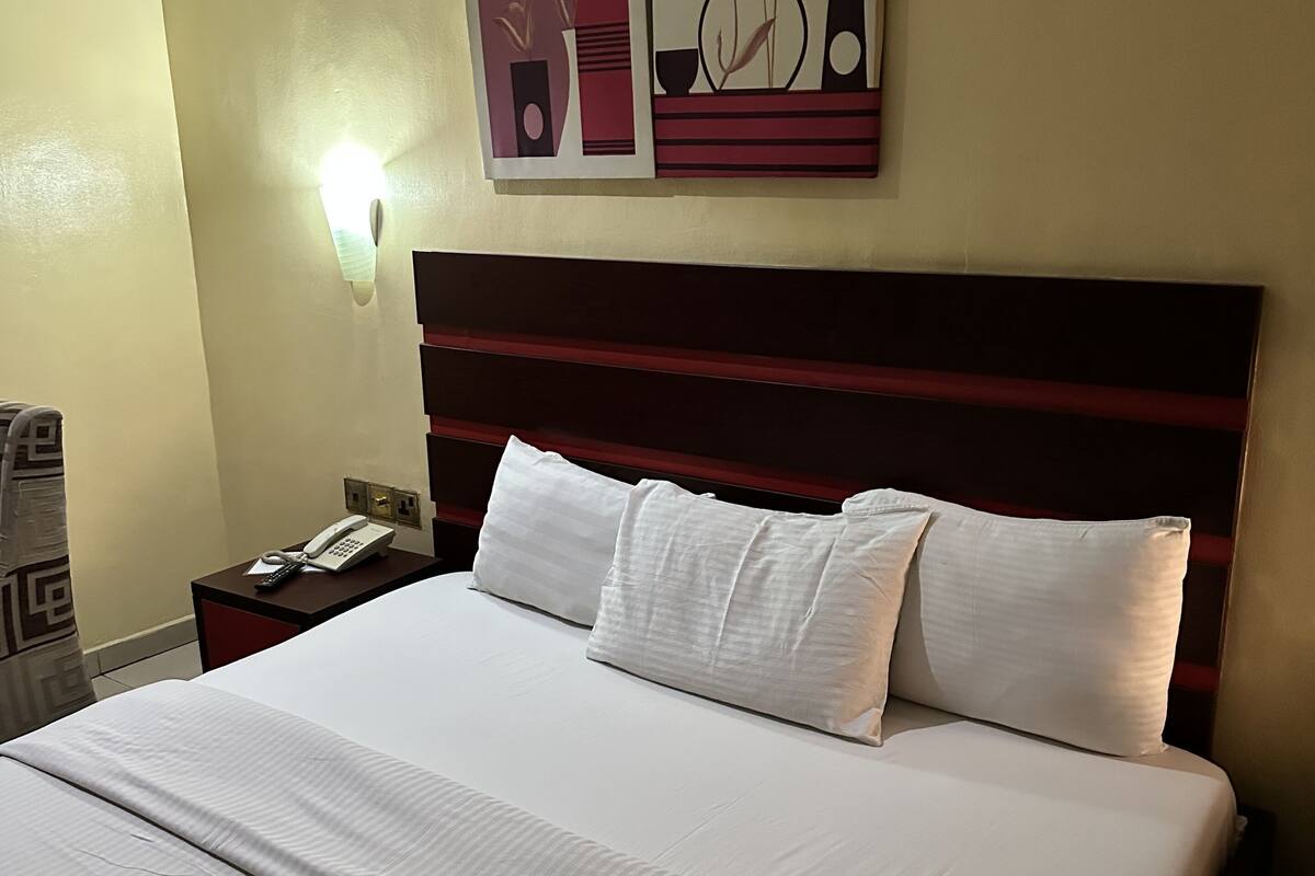 A hotel room with a large bed, a nightstand with a phone, and two wall art pieces.