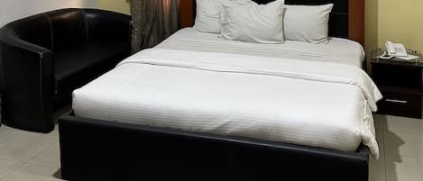 Una cama con cabecera de madera, un banco negro y un teléfono sobre una mesita de noche.