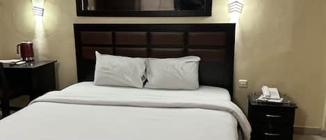 A hotel room with a large bed, a bedside table with a lamp, a nightstand with a phone, and a mirror above the bed.