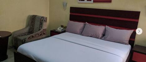 A hotel room with a bed, a chair, a nightstand, and a wall with artwork.
