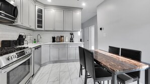 Una cocina moderna con armarios blancos, estufa de acero inoxidable y una zona de comedor con mesa de mármol y sillas negras.