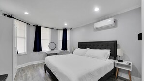 Un dormitorio moderno con una cama grande, una mesita de noche con lámpara y un aire acondicionado de pared.