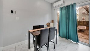Un comedor con mesa y sillas, un equipo de aire acondicionado y vista al patio trasero a través de un ventanal.