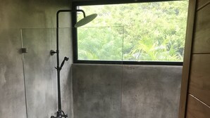 Un bagno con WC, doccia e una finestra vista verde.