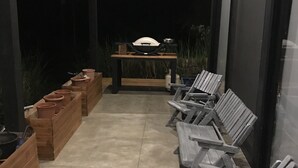Area esterna con panche di legno, fioriere, un barbecue e un tavolo con sedie.