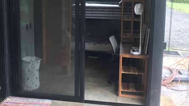 Una camera moderna con un letto, una scrivania e una sedia. Si vede del verde dalla finestra.