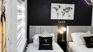 Ein modernes Hotelzimmer mit zwei Betten, einem Wandbild einer Weltkarte und einem 'LUXE'-Schild.
