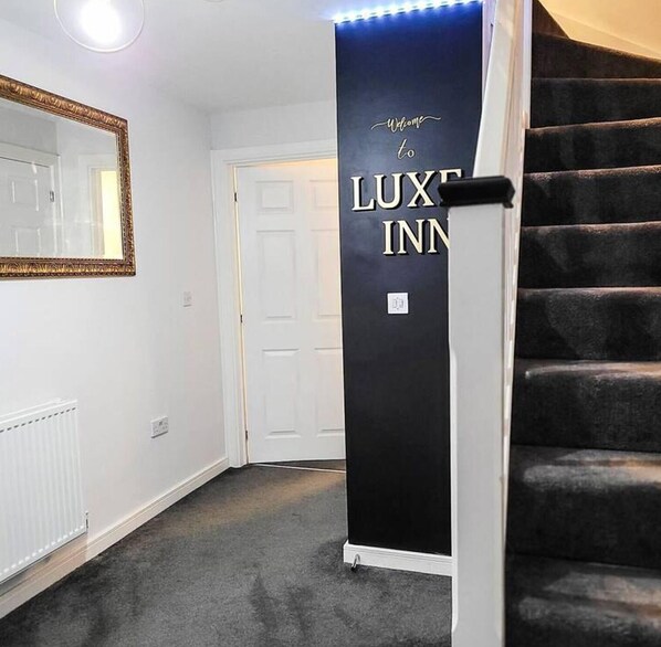 A hallway with a black sign reading "Welcome to LUXE INN" and a mirror on the wall. - Birmingham Airport Luxury3brhome (Birmingham)