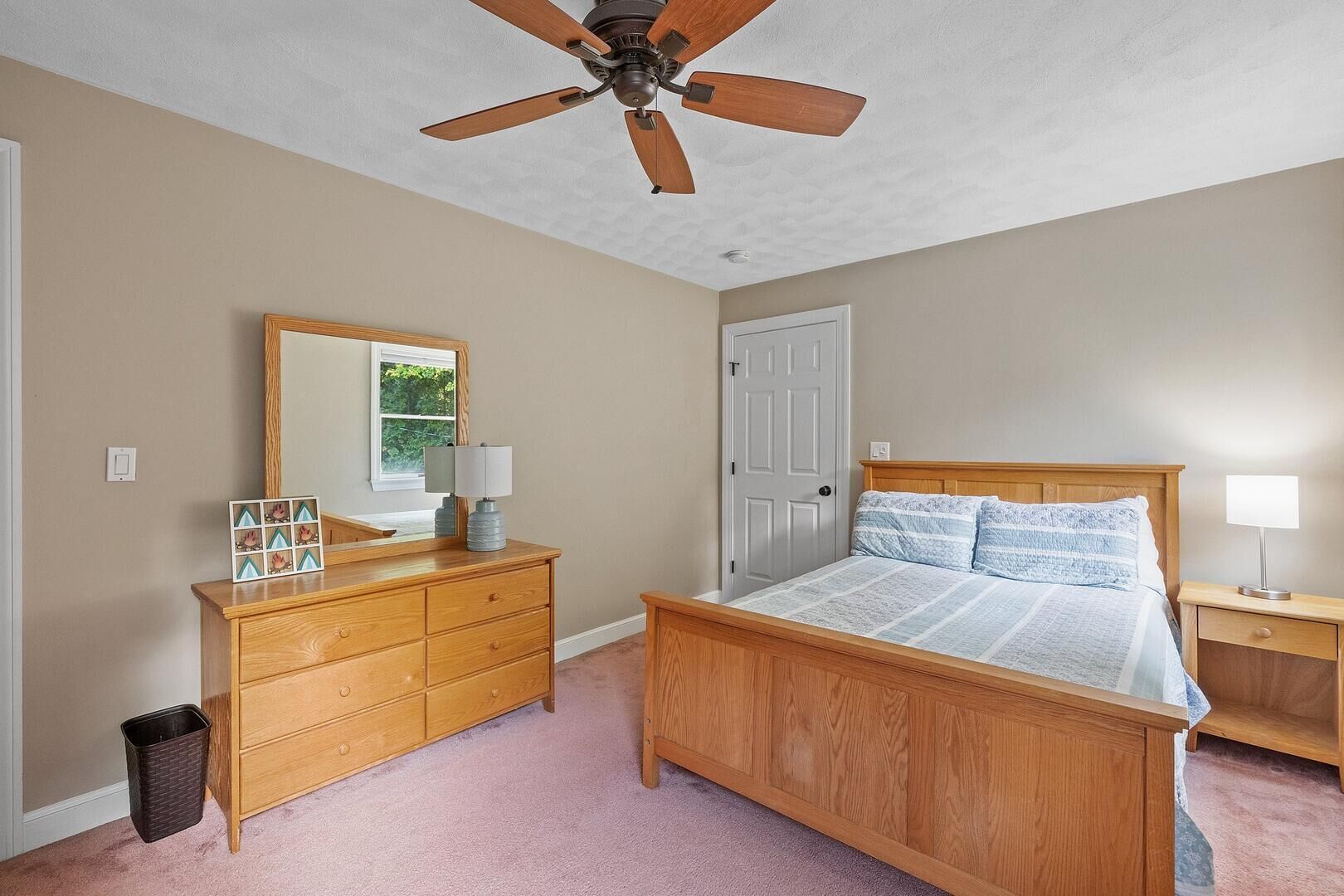 A bedroom with a wooden bed, a dresser, a ceiling fan, and a door.