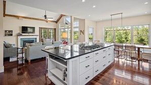 A spacious kitchen with a central island, wooden beams, and large windows offering a view of the outdoors.