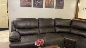 Ein braunes Ledersofa in einem Wohnzimmer mit einer Vase voller rosa Blumen auf einem Holztisch.