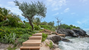 Eine Holztreppe führt zu einem Strand mit felsigem Ufer und Brandwellen.