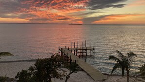 Ein Sonnenuntergang über einem ruhigen Meer mit einem hölzernen Steg und Palmen.