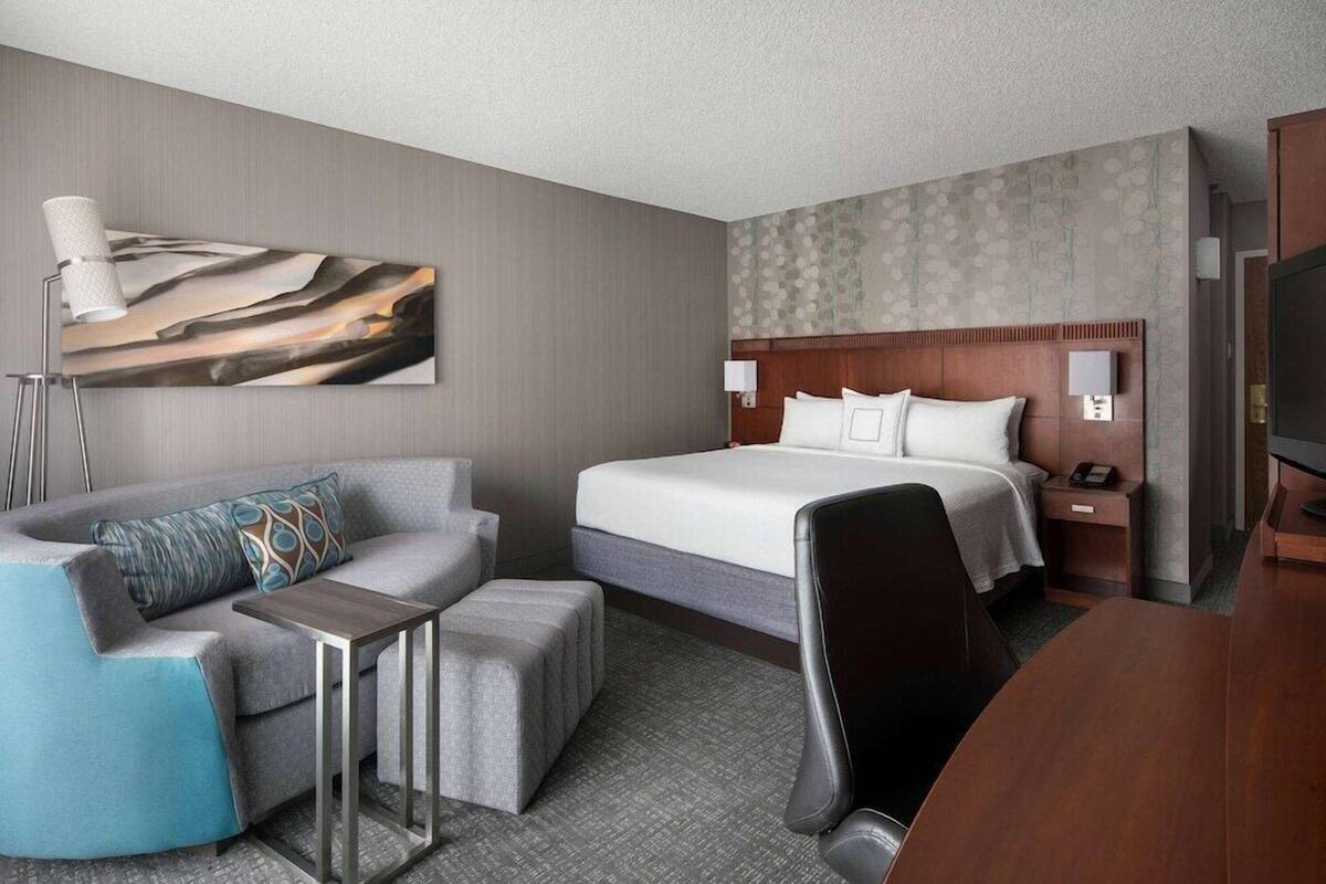 A hotel room with a bed, a desk, a chair, a sofa, and a TV.