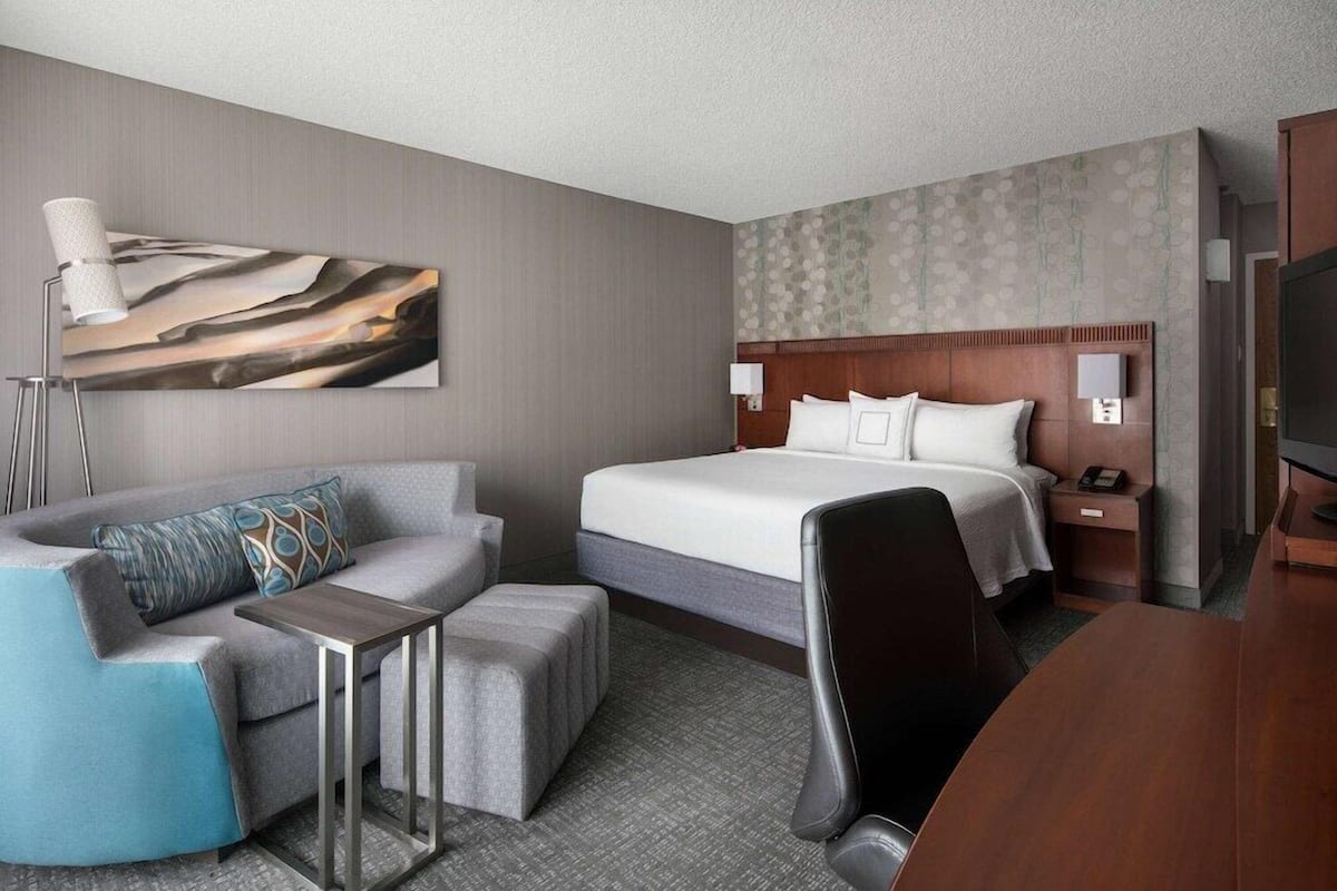 A hotel room with a bed, a desk, a chair, a sofa, and a TV.