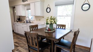 A dining area with a wooden table and chairs, a vase with flowers, and a kitchen in the background. - 2 E-Bikes & Kayaks included & No Cleaning Fees!! (Clear Lake)