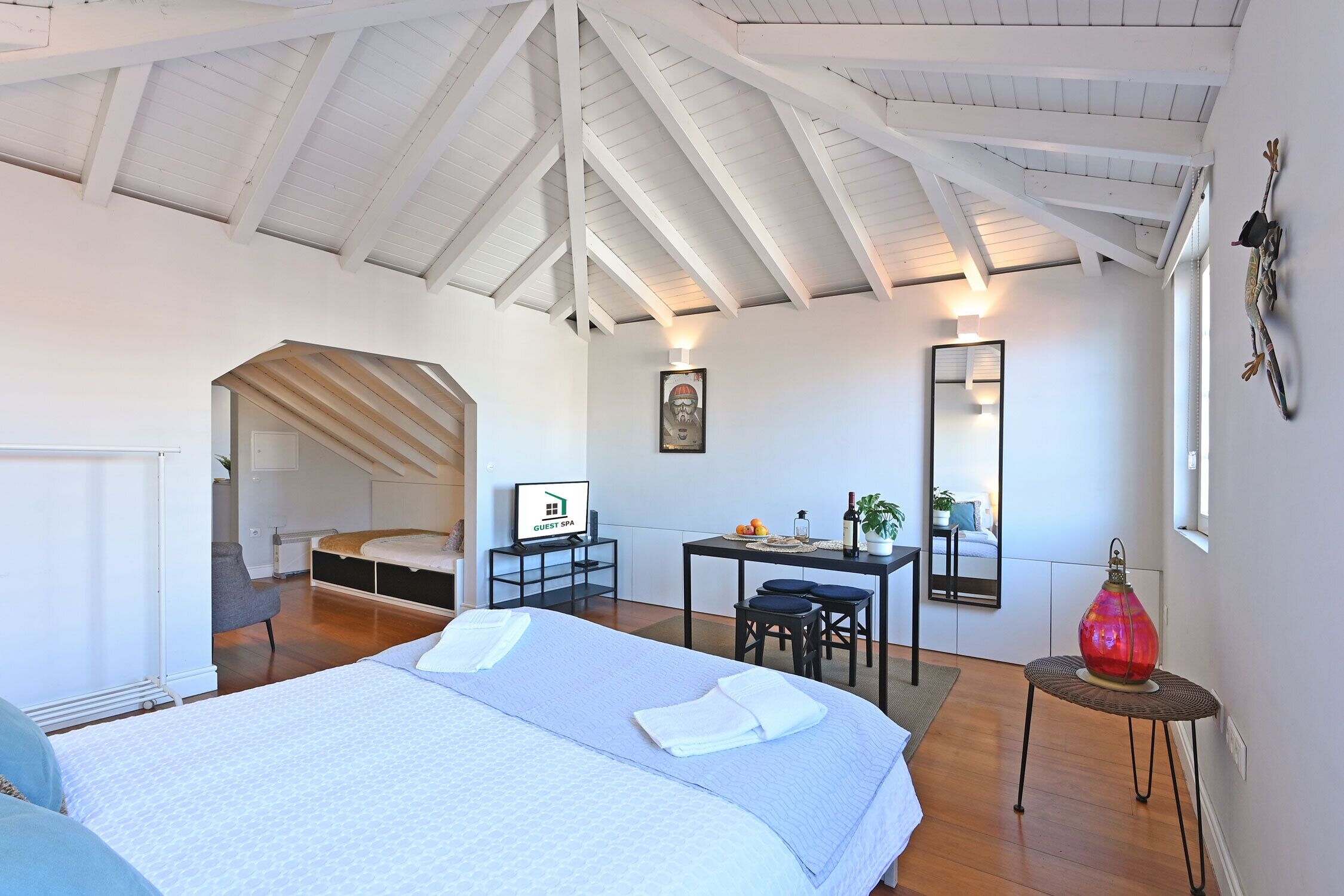 Een hotelkamer met een bed, bureau, stoel en een klein tafeltje met een lamp.