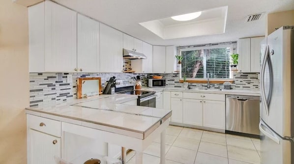 Une cuisine moderne avec des meubles blancs, un îlot central, un four à micro-ondes et un réfrigérateur.
