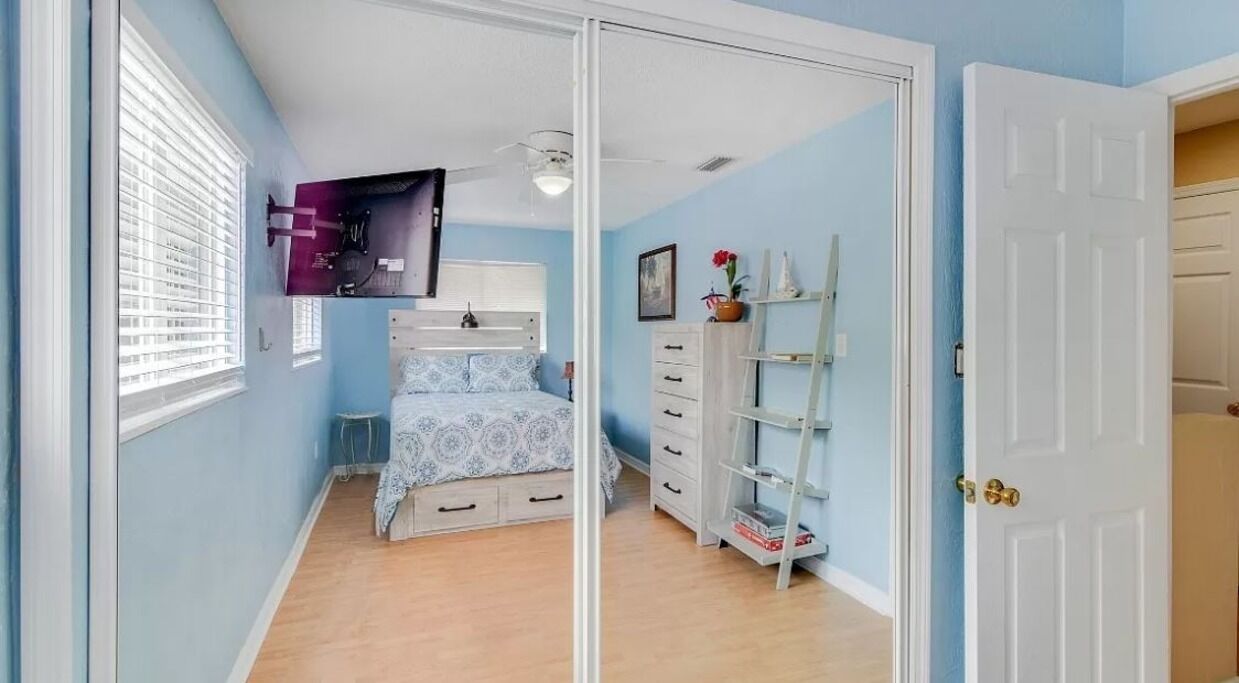 Une chambre à coucher comprenant un lit, une commode, une étagère avec des objets décoratifs et une porte.