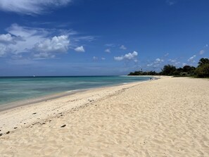 Ein weiter Sandstrand mit klarem türkisblauem Wasser, ein Leuchtturm in der Ferne und einige Personen, die entlanggehen.