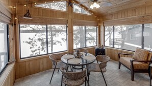 A cozy room with wooden walls, large windows, a ceiling fan, and a round table with chairs.