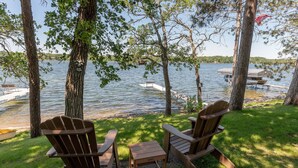 A lakeside setting with two Adirondack chairs, a small table, and a dock extending into the water.