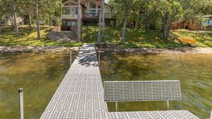 A wooden dock leading to a house with a balcony, surrounded by trees and a body of water.
