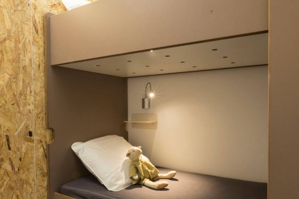 Un lit superposé avec une table de chevet et une lampe, dans une pièce aux murs en bois et au plafond blanc.