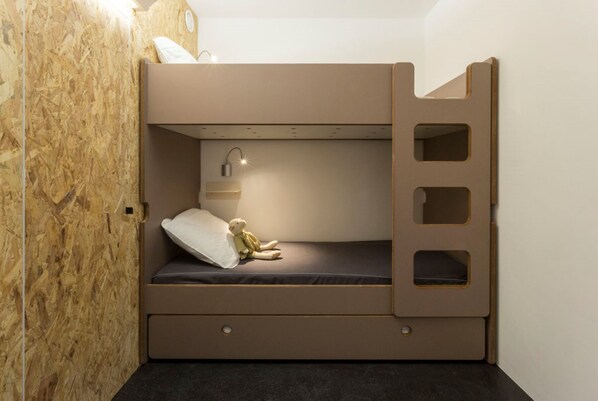 Una cama litera con cabecera, una lámpara de noche y una pequeña estantería.